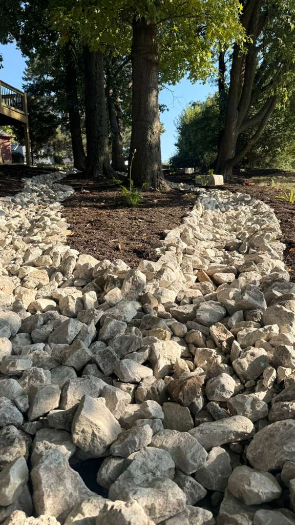 Rock drainage channel installed around mature trees on a sloped Grandview property